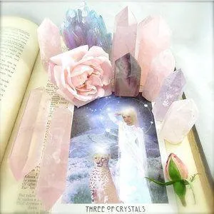 Tarot Card on book surrounded by roses and crystals
